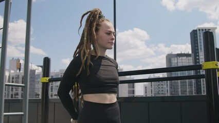 Side tilt footage of Caucasian woman with dreadlocks and lean body stretching legs before safe workout at rooftop recreation ground
