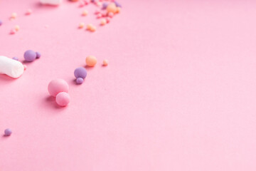 Small candies and marshmallows of different colors and sizes lie on a pink background.  Lots of empty space