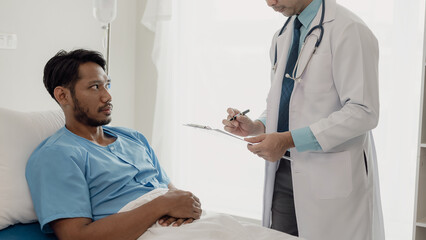Doctor talking with patient in hospital, male patient lying in bed and doctor providing care,...