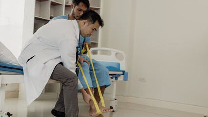 Physiotherapist doing physical therapy on male patient with leg muscle injury in nursing...