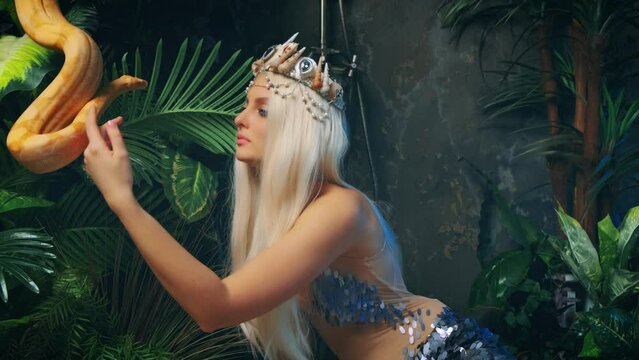 fashion model posing close-up art portrait woman with snake. Girl goddess touches white milk Boa constrictor. Fantasy asp girl white blonde long hair, looks at serpent. Lady queen. green palants 4k