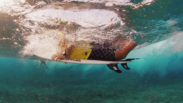 Surfer in yellow shirt dives under the wave with surfboard in the Maldives