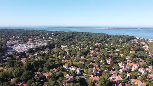 Drone shot panning from left to right showing the houses, trees and the seaside from the distance of the small town of Arcachon in the South of France on a sunny day with clear and blue sky in autumn
