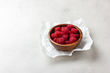 Raspberries in a wooden bowl on a light grey background