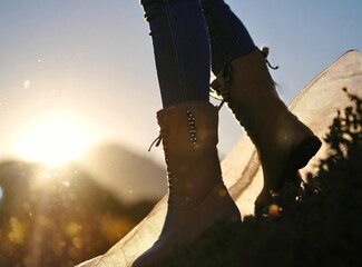Cowboy boots closeup. Girl walking on the mountain, with the sun rising over the horizon.