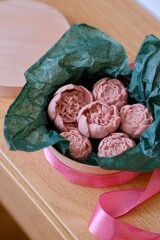 Beautiful pink vegan chocolates in the shape of flowers in a wooden gift box with green paper. An original exquisite unusual romantic gift. Healthy sweets made from coconut milk, cashews, raspberries.