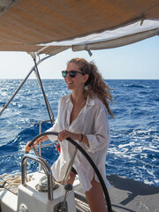 Beautiful blond female skipper at the helm sailing on a yacht in the Mediterranean Sea