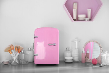 Cosmetics refrigerator and skin care products on grey vanity table indoors
