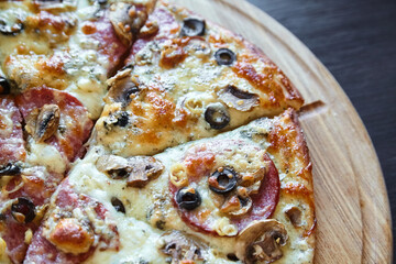 Sliced pepperoni and mushroom pizza with black olives and melted cheese, served on a wooden pizza board on a dark table