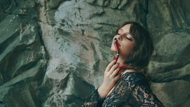 fashion woman posing with snake, portrait close-up Gothic fantasy woman dark queen. Girl holds in hands plays with aspred snake sinaloa. Lady vampire, black dress. Royal milk snake crawls on skin face