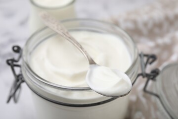 Delicious natural yogurt in glass jar and spoon on table, closeup