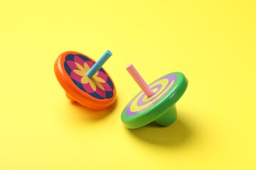 Two colorful spinning tops on yellow background, closeup