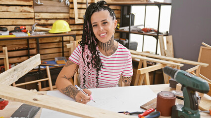 Confident, smiling hispanic woman, an amputee carpenter, drawing confidently with pen at her...