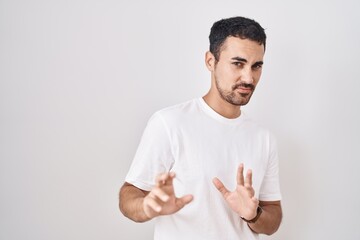 Handsome hispanic man standing over white background disgusted expression, displeased and fearful doing disgust face because aversion reaction.