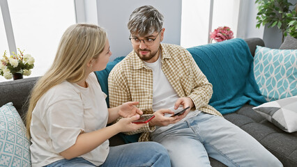 A man and woman sitting on a couch engaging with smartphones in a modern living room.
