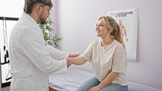 A smiling woman patient at a rehabilitation clinic holds hands with her male physiotherapist in a consultation room.