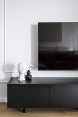 Vase with flower and statuette on wooden tv stand and modern lcd panel on wall