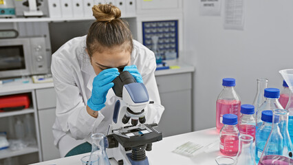 Young beautiful hispanic woman scientist using microscope analysing sample at laboratory