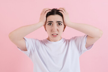 Shocked or stressed attractive caucasian young brunette woman in casual clothing, looking nervously at the camera isolated on a pink studio background.