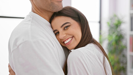 A woman and man in a loving embrace, smiling indoors with a bright home interior in the background.