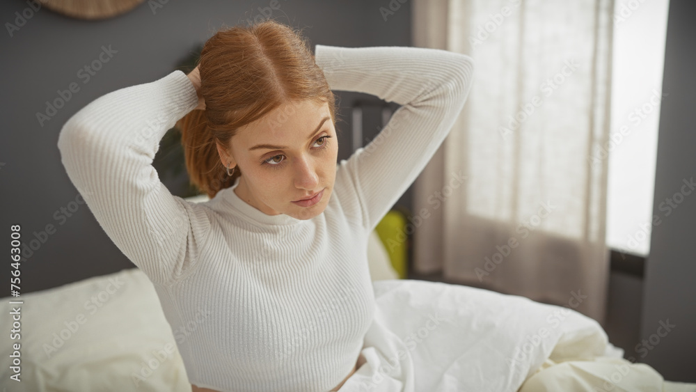 Wall mural A thoughtful young woman with redhead in a white sweater posing in a bedroom setting