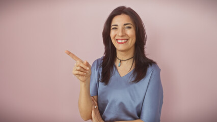 Smiling hispanic woman pointing in casual attire against pink background
