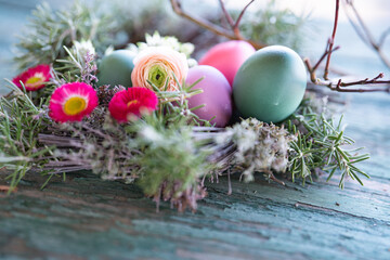 Fototapeta na wymiar Colorful easter eggs in a herb nest with spring flowers on weathered rustic wooden table. Background with short depth of field. Close-up.