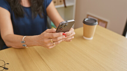 A middle-aged woman engages with a smartphone in an office setting with a coffee cup and glasses.