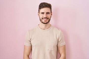 Hispanic man with beard standing over pink background with hands together and crossed fingers smiling relaxed and cheerful. success and optimistic