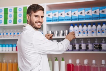 Young caucasian man pharmacist smiling confident holding product on shelving at pharmacy