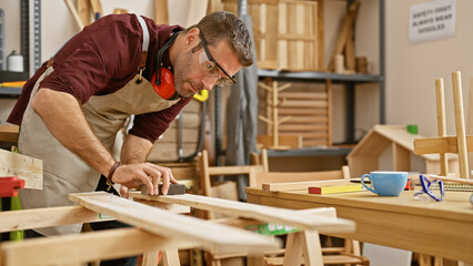 A skilled man measuring wood in a well-equipped carpentry workshop, displaying craftsmanship and focus.
