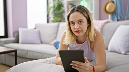 Fototapeta premium Young blonde woman using touchpad lying on sofa at home