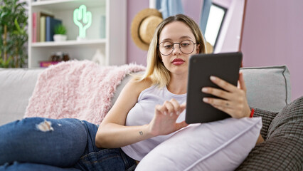 Young blonde woman using touchpad sitting on sofa at home