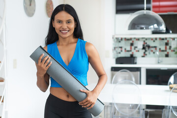 Laughing hispanic woman with yoga mat ready for class at gym - obrazy, fototapety, plakaty