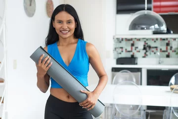 Tuinposter Laughing hispanic woman with yoga mat ready for class at gym © Daniel Ernst