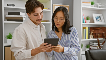 A man and woman collaboratively working over a tablet in a modern office setting, embodying a professional team environment.