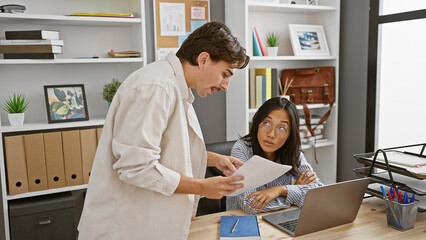 Obraz premium A man and woman discussing documents in a modern office, indicating teamwork and corporate collaboration.