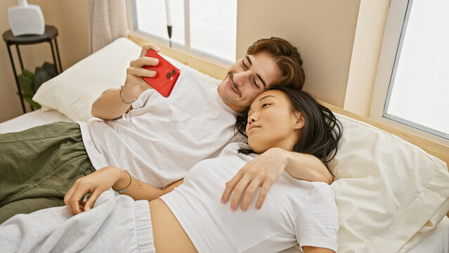 A loving interracial couple, a man and a woman relaxing together in a cozy bedroom, capturing a selfie