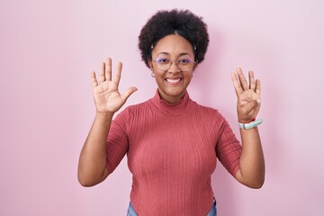 Beautiful african woman with curly hair standing over pink background showing and pointing up with...