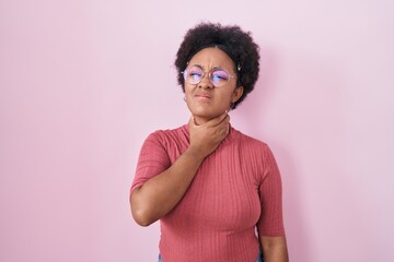 Beautiful african woman with curly hair standing over pink background touching painful neck, sore throat for flu, clod and infection