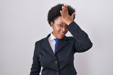 Beautiful african woman with curly hair wearing business jacket and glasses surprised with hand on...