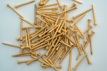 A pile of natural wood colour 70mm bamboo golf tees lying on a white surface