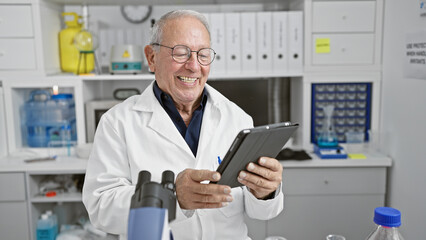Naklejka na ściany i meble Senior man scientist smiling confident using touchpad at laboratory