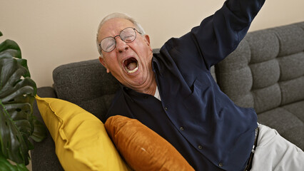 Caught in a cozy moment, portrait of a tired elder man with white hair and glasses waking up with a...