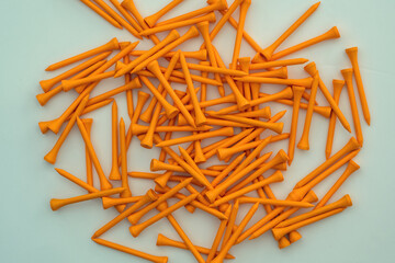 A pile of neon orange 70mm wood golf tees lying on a flat white surface