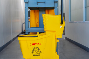 A well-equipped janitorial cart complete with a yellow mop bucket and caution sign, ready for office cleaning tasks. Closeup front shot.