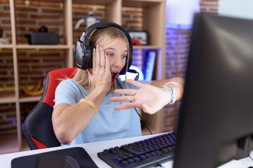 Young caucasian woman playing video games wearing headphones looking at the watch time worried, afraid of getting late