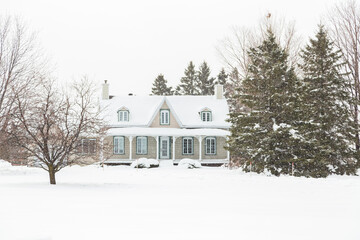 Pretty clapboard house with porch, gable and dormer windows seen during a heavy snowfall in the...