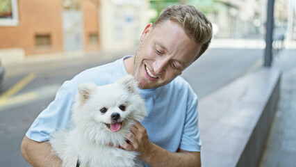 Cheerful young caucasian man confidently smiling while sitting with his joyful puppy on a city bench, enjoying the positive outdoors expression of urban happiness.