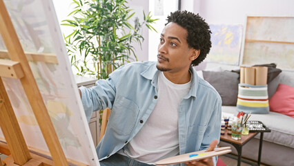 African american man painting on canvas in art studio interior, looking contemplative and creative.
